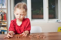 Menina brincando com centavos na mesa — Fotografia de Stock