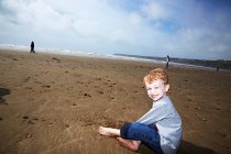 Мальчик сидит на пляже улыбаясь — стоковое фото