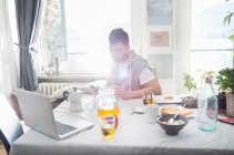 Young man having breakfast and using laptop — Stock Photo