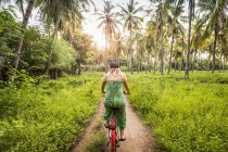 Rear view of young woman cycling in palm tree forest, Gili Meno, Lombok, Indonesia — Stock Photo