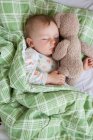 Visão aérea do bebê menino dormindo na cama segurando ursinho de pelúcia — Fotografia de Stock