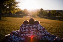 Rear view of three girls wrapped in blanket at sunset — Stock Photo