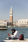 Young woman reading guidebook on waterfront opposite St Marks Square, Venice, Italy — Stock Photo