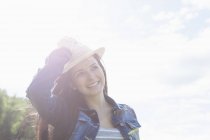 Молода жінка посміхається, тримаючись на капелюсі — стокове фото