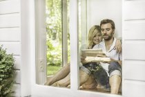 Casal adulto médio sentado no chão e usando tablet digital na janela da casa — Fotografia de Stock