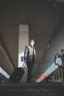 Portrait of young businessman commuter at top of stairs pulling suitcase. — Stock Photo