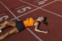 Jeune coureuse couchée sur le dos épuisée sur piste — Photo de stock