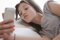 Chica acostada en la cama mirando el mensaje de texto del teléfono inteligente - foto de stock