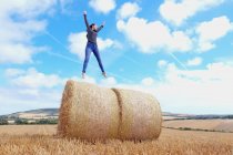 Молодая женщина прыгает на вершину стога сена в собранном поле — стоковое фото
