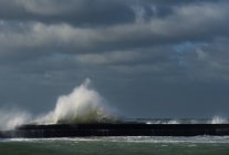 Ciel orageux et vagues océaniques éclaboussant le mur du port — Photo de stock