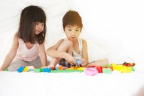 Junge chinesische Jungen und Mädchen spielen im Bett mit ihren Spielzeugen unter den Bettlaken — Stockfoto