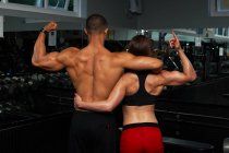 Young woman and mid adult man, flexing muscles, rear view — Stock Photo
