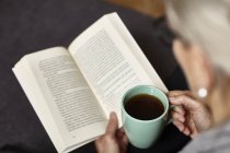 Mulher sênior segurando xícara de café e leitura — Fotografia de Stock