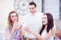 Drei junge erwachsene Freunde stoßen in der Küche mit Weißwein an — Stockfoto