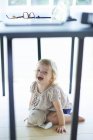 Скрывающийся и смеющийся под обеденным столом ребенок — стоковое фото