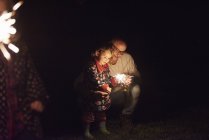 Pai agachado ao lado da filha segurando sparkler — Fotografia de Stock