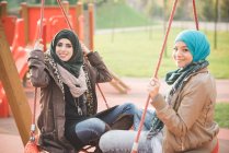 Porträt zweier junger Frauen auf Spielplatzschaukeln — Stockfoto