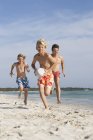 Garçon courir avec ballon de rugby poursuivi par frère et père sur la plage, Majorque, Espagne — Photo de stock
