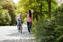 Front view of young smiling woman on bicycle chasing young woman holding panama hat — Stock Photo