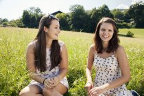 Young cheerful smiling women sitting in field with green grass — Stock Photo