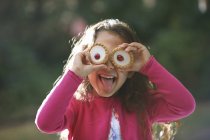 Portrait of girl with tartlets in front of her eyes in garden — Stock Photo