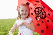 Chica con paraguas rojo en el campo - foto de stock