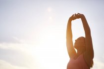 Молода жінка бігунка розтягує руки на сонячне світле небо — стокове фото