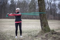 Зрелая женщина тренируется в парке, тянет пояс сопротивления — стоковое фото
