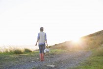 Visão traseira da jovem mulher em pé na colina ao pôr do sol — Fotografia de Stock