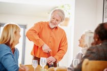Старший чоловік відкриває вино з друзями — стокове фото