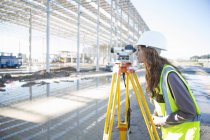 Vermessungsingenieur lehnt sich nach vorne und blickt durch Ebene auf Baustelle — Stockfoto