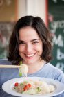 Женщина держит лапшу палочками для еды и улыбается — стоковое фото