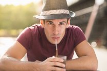Young man wearing hat drinking through straw — Stock Photo