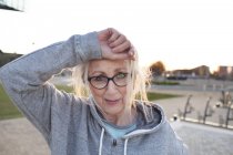 Portrait of woman wearing eyeglasses and hooded top, hand on forehead looking at camera smiling — Stock Photo