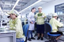 Superviseur supervisant le travail au poste de contrôle de la qualité de l'usine produisant des cartes de circuits électroniques flexibles. L'usine est située dans le sud de la Chine, à Zhuhai, province du Guangdong — Photo de stock
