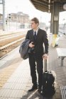 Jovem empresário viajante de pé na plataforma ferroviária com mala . — Fotografia de Stock