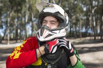 Motocross motorcycle competitor fastening helmet in forest — Stock Photo
