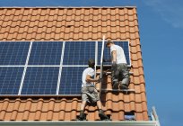 Trabajadores instalan paneles solares en el marco del techo de un nuevo hogar, Países Bajos - foto de stock