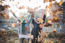 Dos mujeres jóvenes en el parque lanzando hojas de otoño - foto de stock