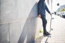 Молодий чоловік міський скейтбордист, що спирається на тротуарну стіну — стокове фото