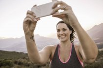 Плюс розмір жінки на горі, використовуючи смартфон, щоб взяти селфі посміхаючись — стокове фото