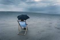 Reife Frau sitzt auf Liegestuhl am stürmischen Strand, unter Sonnenschirm — Stockfoto