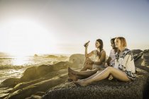 Три середині дорослих, сидячи на пляжі з видом на захід сонця, Кейптаун, Південно-Африканська Республіка — стокове фото
