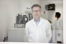 Cientista sorrindo em laboratório, colega trabalhando em segundo plano — Fotografia de Stock