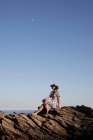 Девушка, сидящая на скалах у моря — стоковое фото