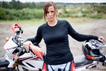 Portrait of young adult female motorcyclist leaning on motorcycle — Stock Photo