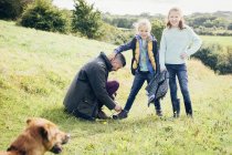 Father tying daughters shoelace in countryside field — Stock Photo