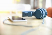 Сині навушники, прикріплені до смартфона на столі — стокове фото