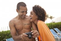 Couple laughing at photographs on digital camera at hotel poolside, Rio De Janeiro, Brazil — Stock Photo