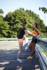 Two young female runners tying trainer laces in parking lot — Stock Photo